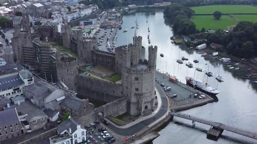 Ancient Caernarfon castle Welsh harbour town aerial view medieval waterfront landmark quick zoom in