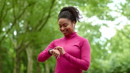 Young Positive African American Woman in Headphones Using Smartwatch Choosing Music for Run Workout