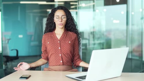 Young businesswoman is meditating with her eyes closed sitting at a workplace in the office. Happy