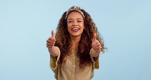 Face, smile and thumbs up of woman in studio isolated on a blue background mockup space