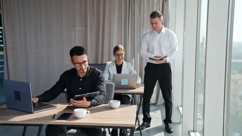 Office work in the light room. Male manager stands near female employee showing her paper notebook.