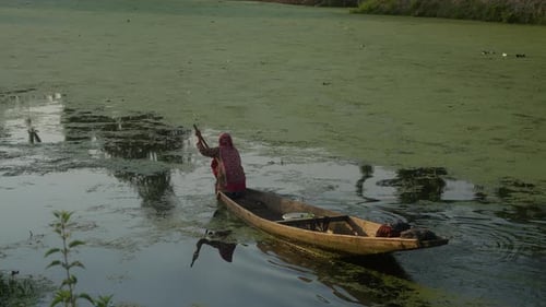 Woman Paddling Boat through Algae-Covered Waterway