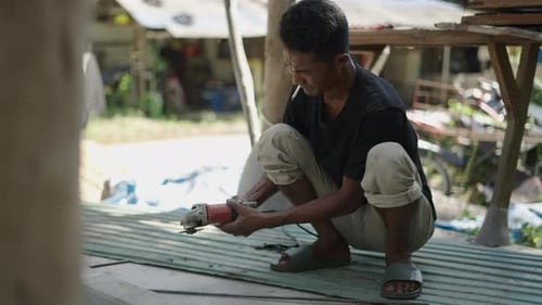Adult Asian Man Using a Disk Grinder While Smoking with No Protection