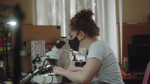 Arbeiterin in einem Servicecenter benutzt Mikroskop und elektronische Leiterplatte Mädchen sucht