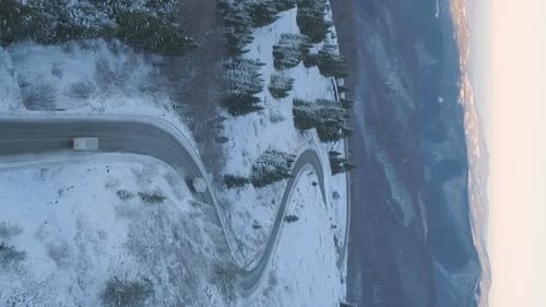 Vertical Video of Drone Follows Delivery Trucks Through a Mountain Pass in a Snowy Setting