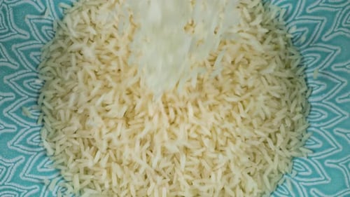 Long grain rice is poured into a ceramic blue bowl. Top view. Slow motion.