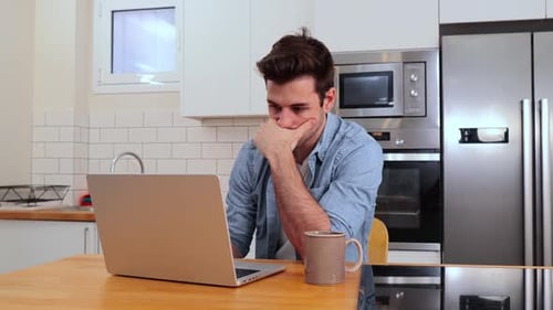 Pensive Man Working on Laptop in Bright Kitchen