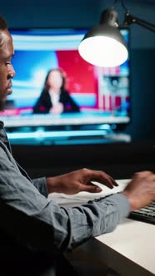 Man Working on Computer Watching News Broadcast