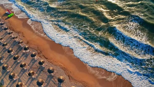 Aerial drone shot of a tropical beach at sunset. View of the wooden umbrellas and sun beds at the be