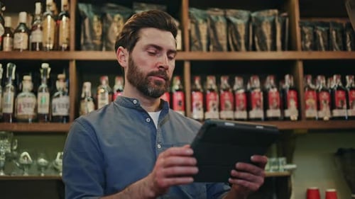 Handsome Man in Uniform Standing at Bar Counter and Tapping on Tablet Screen