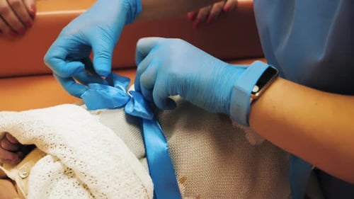 Concept of Newborn Boy Birthday Celebration Nurse Tying Blue Ribbon Bow