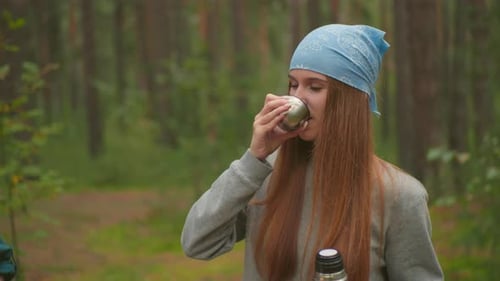 Young Woman Enjoying Warm Drink From Thermos in Peaceful Forest