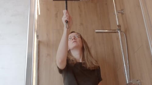 Woman Cleaning Glass Shower Door with Squeegee in Bathroom