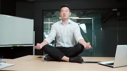Asian business man meditating. Successful businessman meditates sitting at table in modern office,