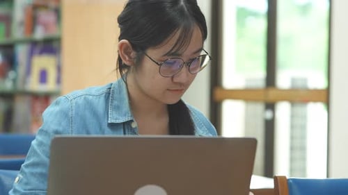 Junge Studentin studiert auf ihrem Laptop in der Bibliothek