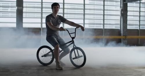 Sportsman Sitting on BMX in Parking Lot with Smoke During Training