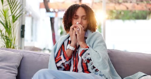 Woman Blowing Nose Wrapped in Blanket at Home