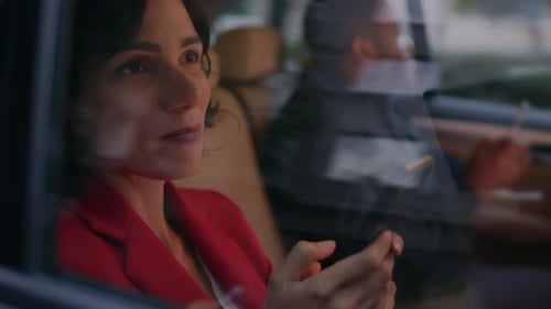 Young Woman and Man Riding on the Backseat of a Car in the Evening. They Both Use Smartphones, Brow