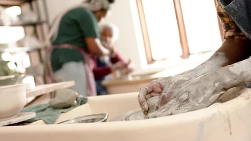 Mains d'un potier afro-américain utilisant un tour de potier dans un studio de poterie, Ralenti