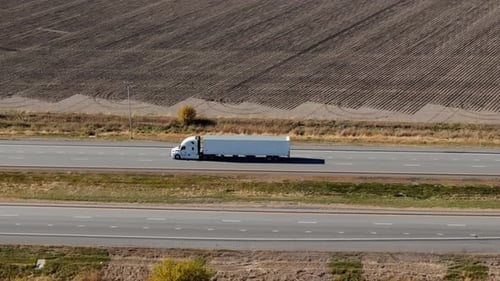 Drone View of Delivery White Truck Driving Forward on a Scenic State Highway Close to the Farm Field