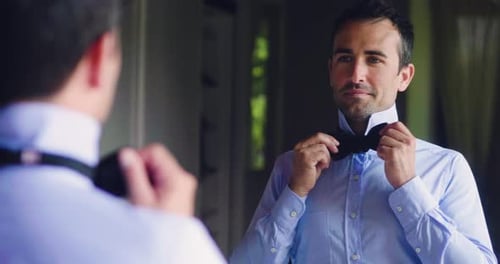 Slow motion of smiling man is tying a papillon in front of the mirror in bedroom for preparing for