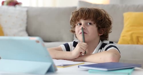 Nachdenklicher Junge mit Tablet macht Hausaufgaben am Tisch im Zimmer