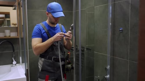 Young Handsome Plumber in Uniform Fixing the Shower