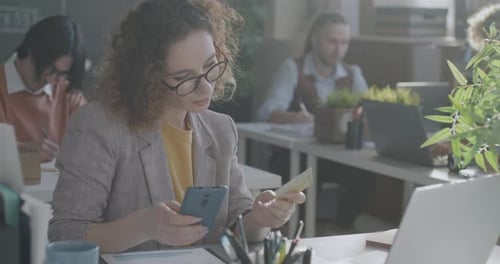 Young Businesswoman Using Smartphone and Credit Card Smiling Enjoying Mobile Banking in Office