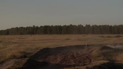 Dirtbike Rider Racing Through Rural Landscape at Sunset