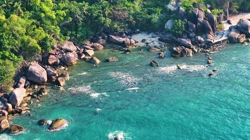 Aerial drone view of foamy waves breaking on a rocky shore.