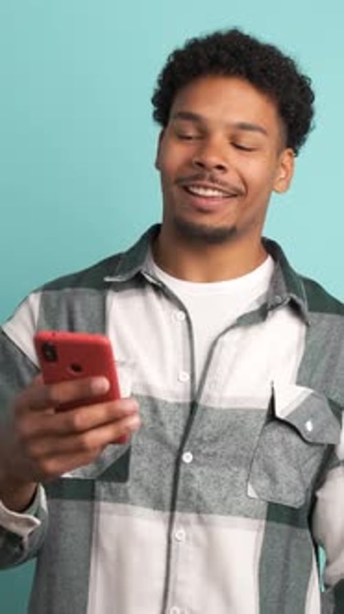 Smiling Young Man Using Smartphone in Blue Studio