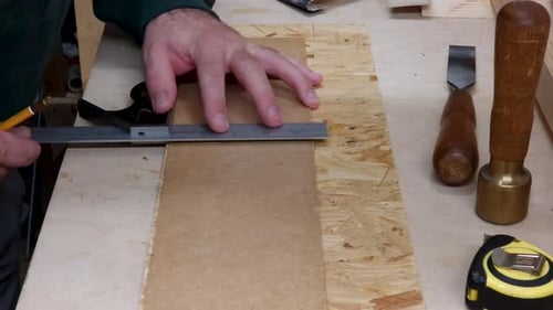 A joiner marks a workpiece using a right-angle and a tape measure.