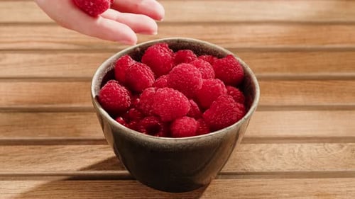 Fresh Raspberries Poured into Bowl on Wooden Table
