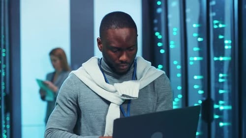 Ein Mann mit Gesichtsbehaarung benutzt einen Laptop in einem Serverraum