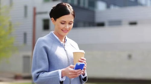 Young businesswoman smiling texting and drinking coffee in the city