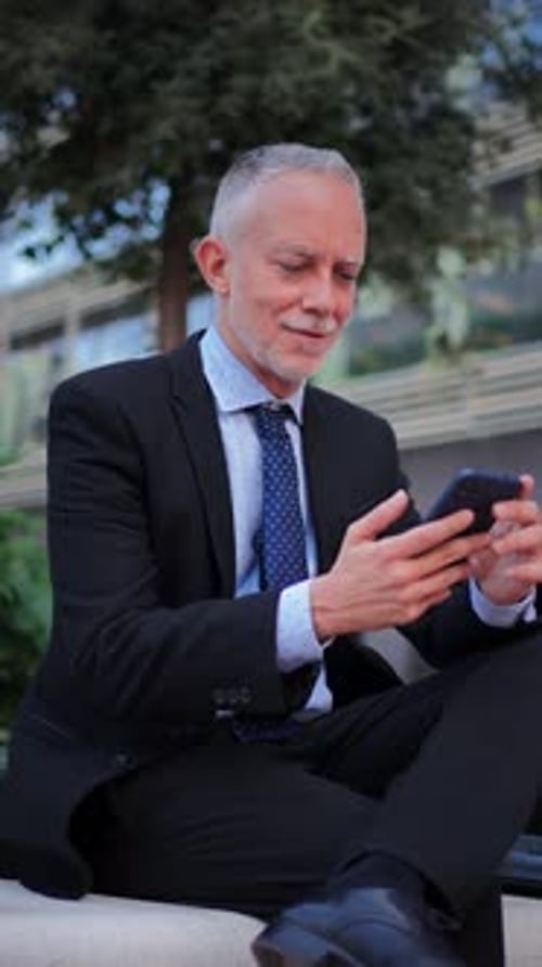 Confident Businessman Using Smartphone While Sitting on a Step in a Professional Attire Outdoors
