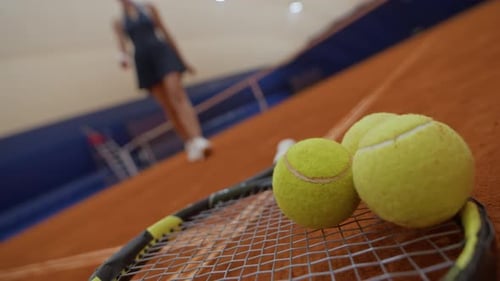 Woman Picking up Racket from Clay Court while Playing Tennis Indoors