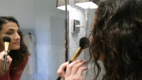 Woman Applying Makeup with Brush in Bathroom Mirror