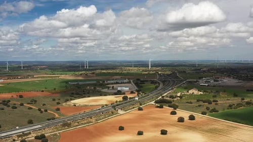 Aerial View of Highway Junction Crossing Farmland with Wind Turbines Under Cloudy Sky