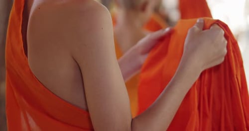 Person in Orange Robes Adjusting Fabric