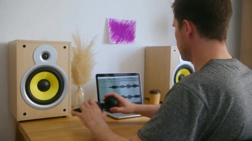 A Man in a Home Music Studio Sits at a Desk with Equipment and Stuck Using the Laptop