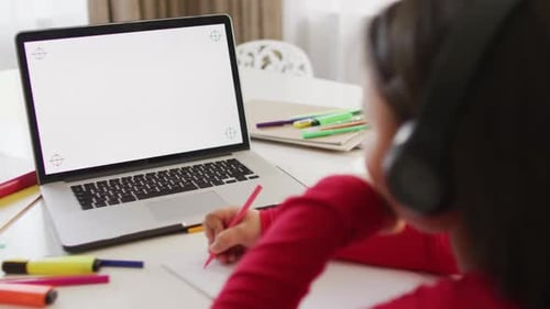 Child Writes at Desk with Laptop and Headphones