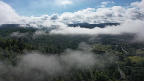 Drone footage of a serene mountain landscape blanketed in dense morning fog, with clouds slowly reve