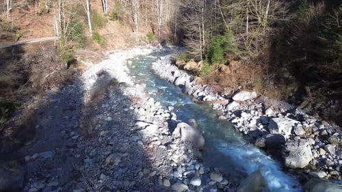 Drohne folgt einer Bergstraße mit kristallklarem Fluss daneben in Europa Österreich