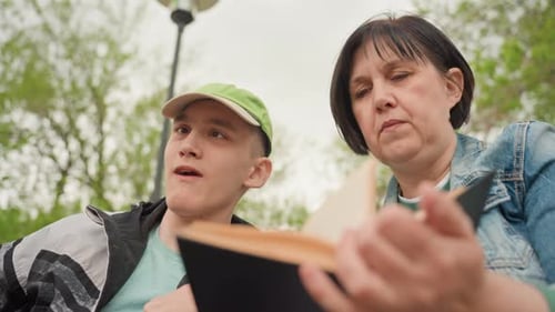 Teenage Boy and Woman Reading Together in Park