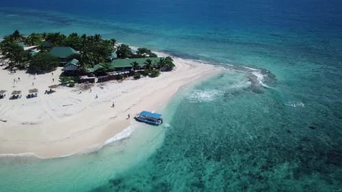 Aerial shot descending over Southsea island exotic paradise in Fiji, with people walking towards a b