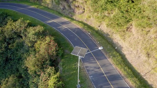 Solar-powered street light on curved road in green hillside