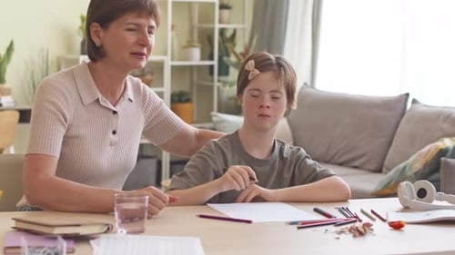 Woman Helping Child Drawing Indoors at Table