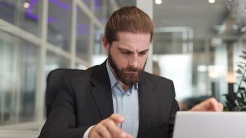 Hombre nervioso que sostiene una carta de papel mientras está sentado en la mesa con una computadora portátil en la oficina