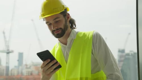 Engenheiro capataz com capacete de segurança e colete usando smartphone